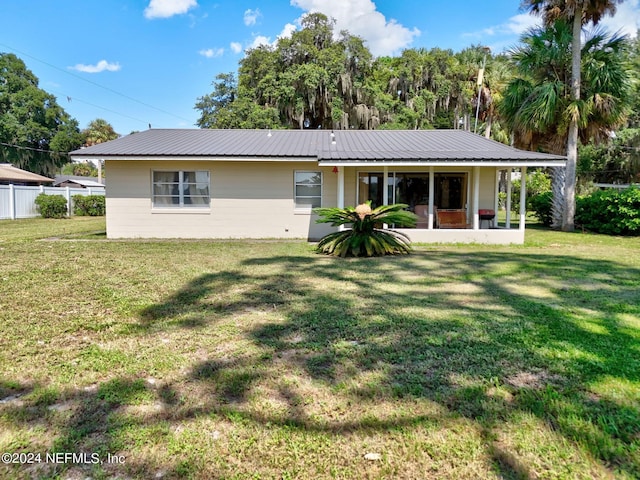 back of property featuring a sunroom, metal roof, a lawn, and fence