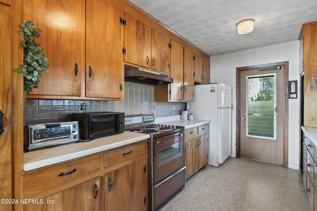 kitchen with range, brown cabinetry, freestanding refrigerator, light countertops, and under cabinet range hood