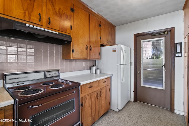 kitchen with range, brown cabinets, freestanding refrigerator, light countertops, and under cabinet range hood