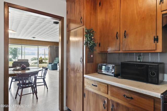 kitchen featuring brown cabinets, a toaster, black microwave, and decorative backsplash