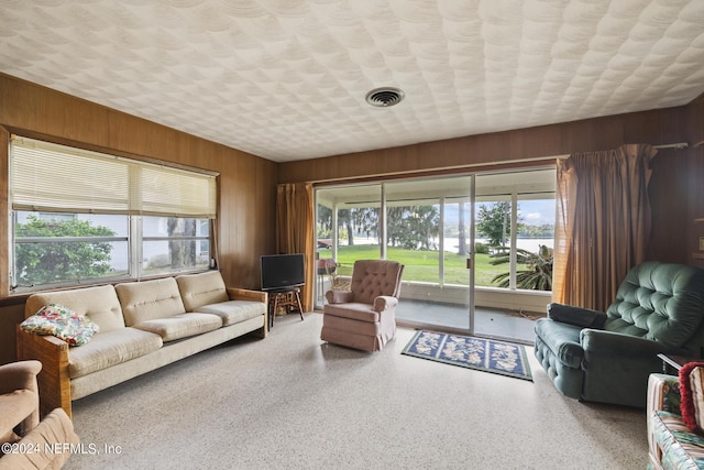 living room featuring a textured ceiling, speckled floor, wood walls, and visible vents