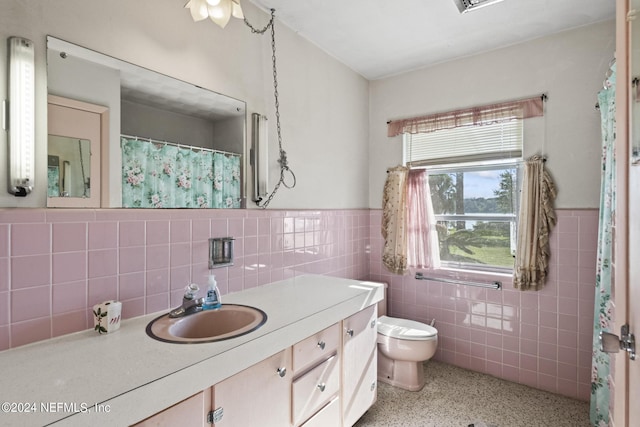 bathroom featuring wainscoting, toilet, vanity, speckled floor, and tile walls