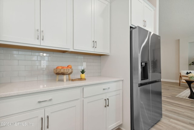 kitchen featuring light wood-type flooring, stainless steel refrigerator with ice dispenser, tasteful backsplash, white cabinetry, and light stone counters