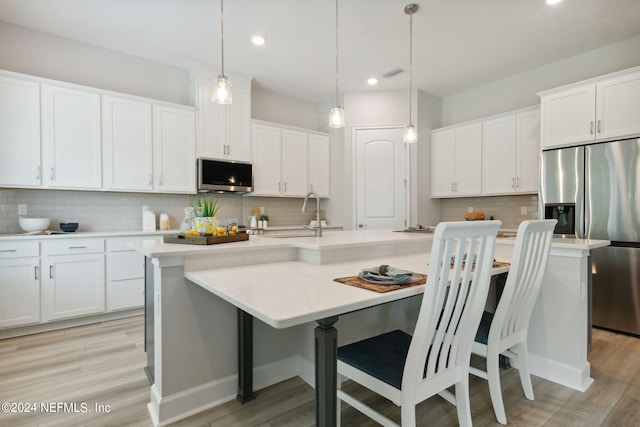 kitchen featuring light wood-type flooring, hanging light fixtures, decorative backsplash, and an island with sink