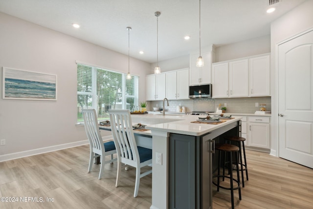 kitchen featuring hanging light fixtures, light hardwood / wood-style flooring, tasteful backsplash, and white cabinets