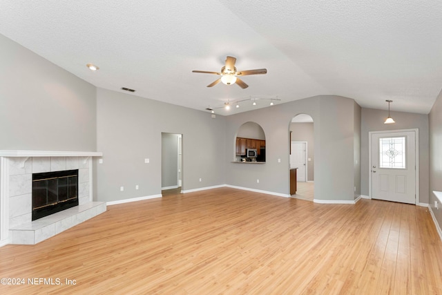 unfurnished living room with a tiled fireplace, vaulted ceiling, light hardwood / wood-style flooring, ceiling fan, and a textured ceiling