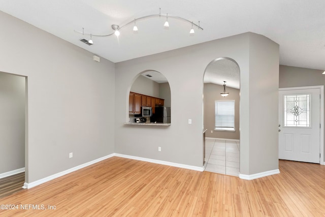 empty room with vaulted ceiling, a textured ceiling, and light hardwood / wood-style flooring