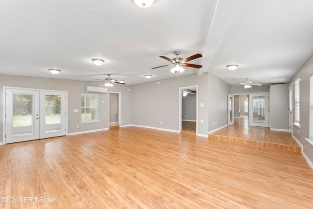 unfurnished living room featuring light wood-type flooring, ceiling fan, a wall mounted air conditioner, and a textured ceiling