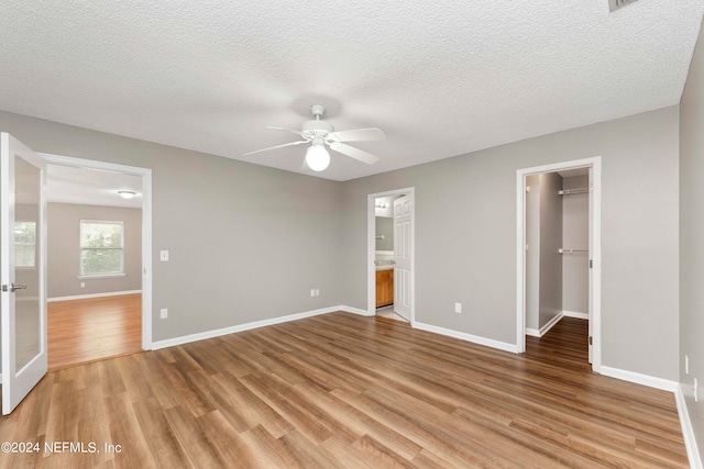 unfurnished bedroom with light hardwood / wood-style flooring, connected bathroom, ceiling fan, a closet, and a walk in closet