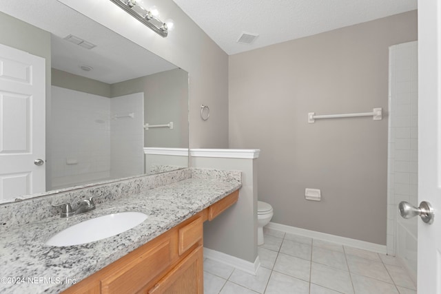 bathroom with a textured ceiling, vanity, tile patterned flooring, tiled shower, and toilet