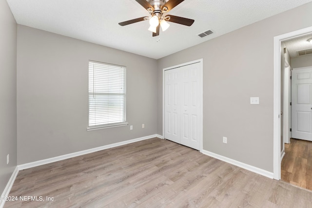 unfurnished bedroom with a textured ceiling, ceiling fan, a closet, and light wood-type flooring