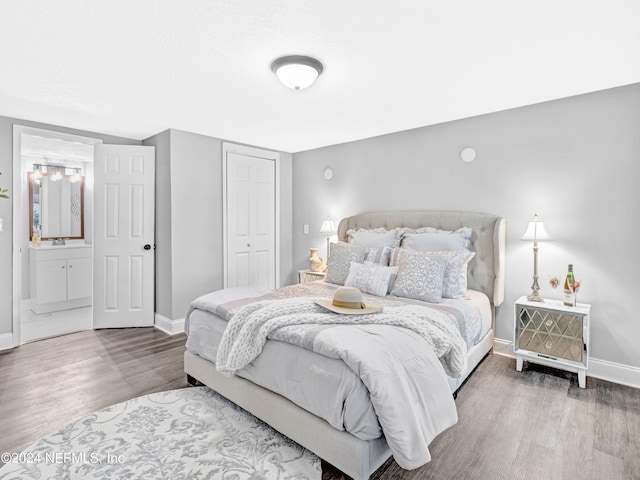 bedroom featuring a sink, wood finished floors, baseboards, a closet, and ensuite bath