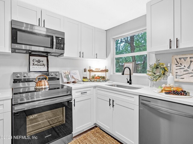 kitchen featuring appliances with stainless steel finishes, white cabinets, light countertops, and a sink