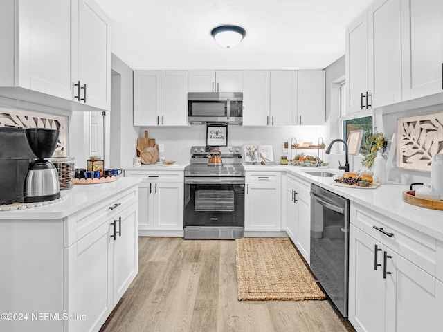 kitchen with stainless steel appliances, light countertops, light wood-style flooring, white cabinetry, and a sink