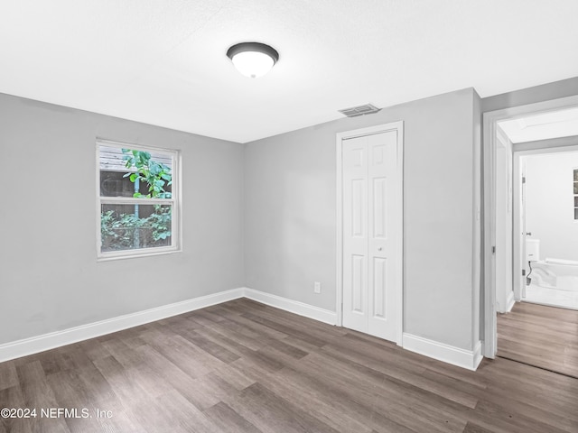 unfurnished bedroom featuring dark wood-style floors, baseboards, visible vents, and a closet