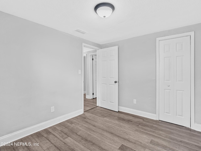 unfurnished bedroom with a closet, visible vents, baseboards, and wood finished floors