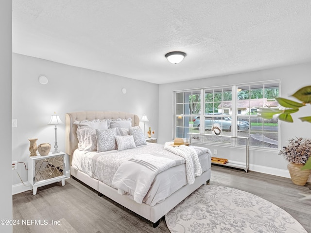 bedroom with a textured ceiling, wood finished floors, and baseboards