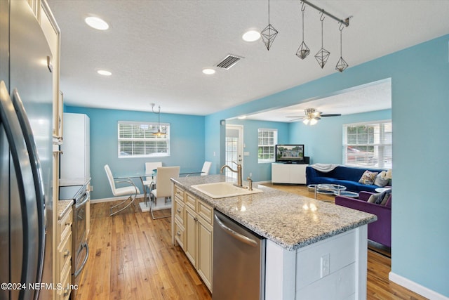 kitchen with light hardwood / wood-style flooring, stainless steel appliances, sink, ceiling fan, and a center island with sink