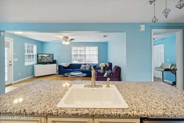 kitchen with ceiling fan, sink, light stone countertops, and light hardwood / wood-style floors