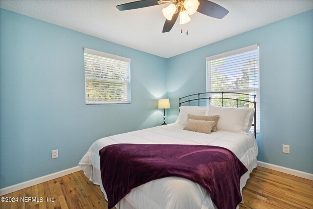 bedroom featuring a textured ceiling, ceiling fan, wood-type flooring, and multiple windows