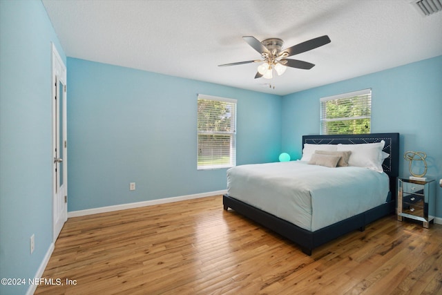 bedroom with visible vents, ceiling fan, a textured ceiling, wood finished floors, and baseboards