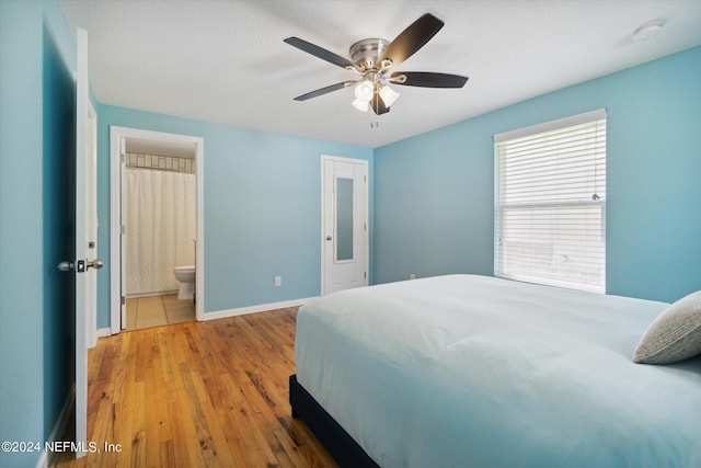 bedroom featuring ceiling fan, ensuite bath, wood finished floors, and baseboards