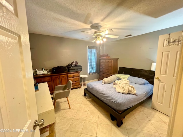 bedroom featuring ceiling fan, light tile patterned floors, and a textured ceiling