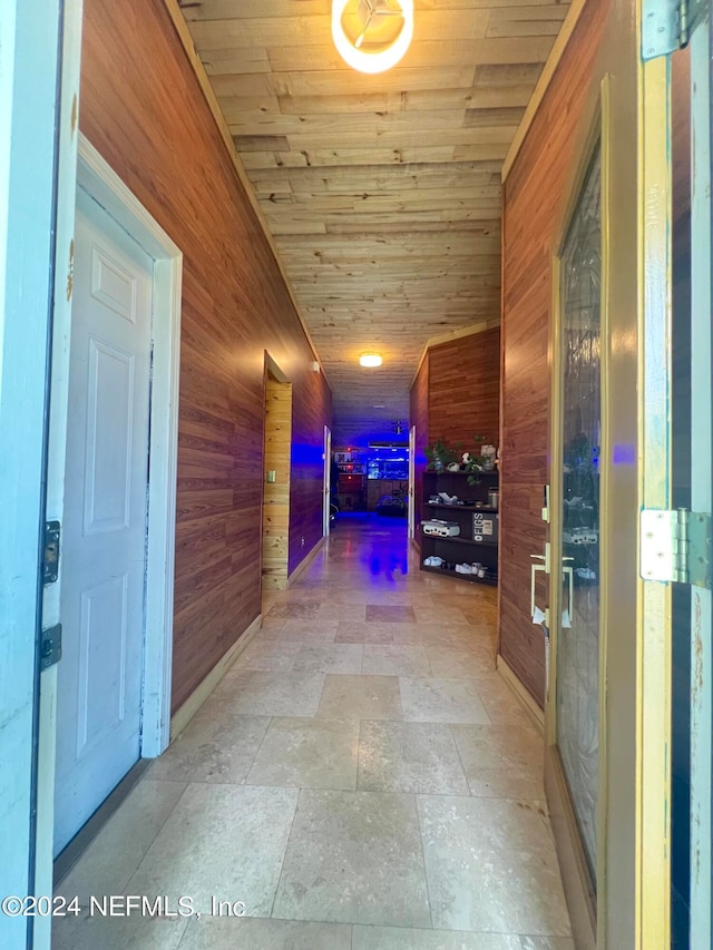 hall with light tile patterned floors, wood ceiling, and wooden walls