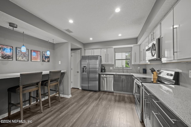 kitchen featuring white cabinetry, stainless steel appliances, hanging light fixtures, and hardwood / wood-style flooring