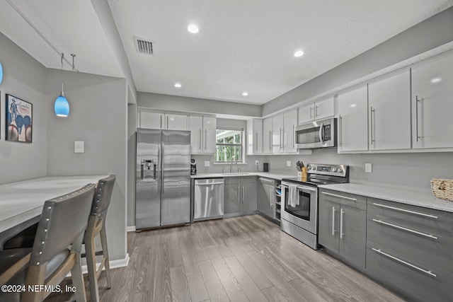 kitchen with hanging light fixtures, light hardwood / wood-style flooring, appliances with stainless steel finishes, sink, and gray cabinets