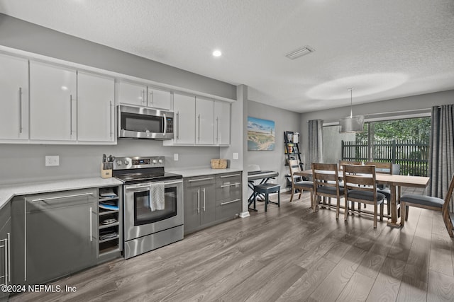 kitchen with a textured ceiling, pendant lighting, wood-type flooring, appliances with stainless steel finishes, and white cabinets