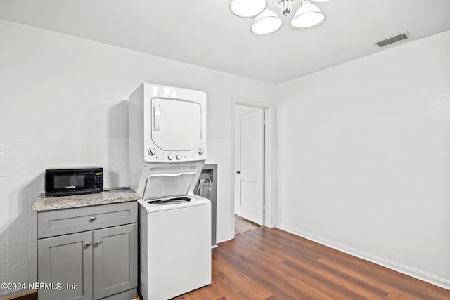 clothes washing area with hardwood / wood-style floors, stacked washer / dryer, and an inviting chandelier