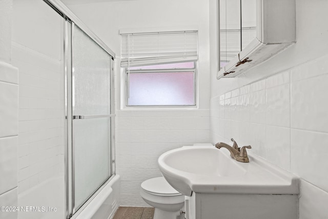 bathroom featuring tile walls, bath / shower combo with glass door, and toilet