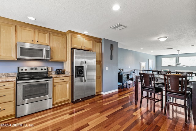 kitchen with a textured ceiling, dark wood-type flooring, light stone counters, and appliances with stainless steel finishes