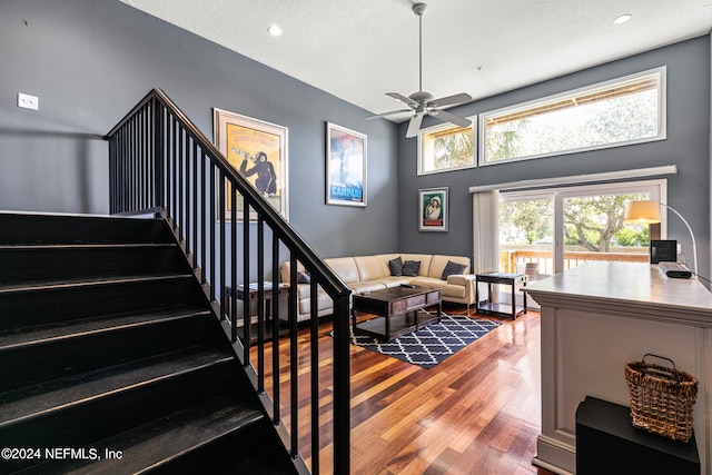 living room featuring a high ceiling, ceiling fan, hardwood / wood-style flooring, and a textured ceiling