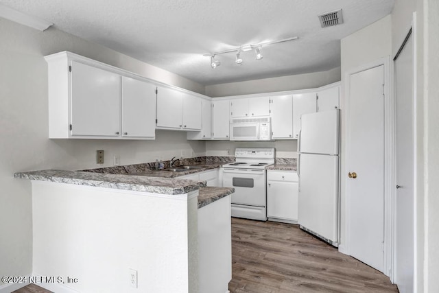 kitchen with a peninsula, white appliances, a sink, visible vents, and white cabinetry