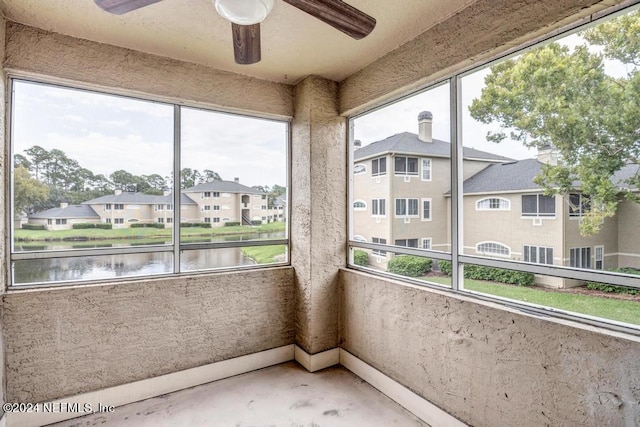 unfurnished sunroom with ceiling fan, a water view, and a residential view