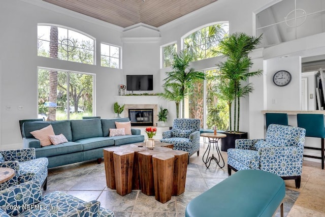 living area featuring ornamental molding, a glass covered fireplace, wood ceiling, and a towering ceiling