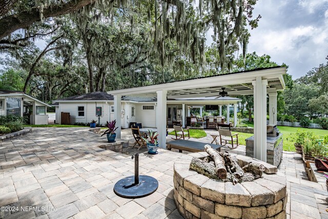 view of patio with ceiling fan, an outdoor structure, and a fire pit