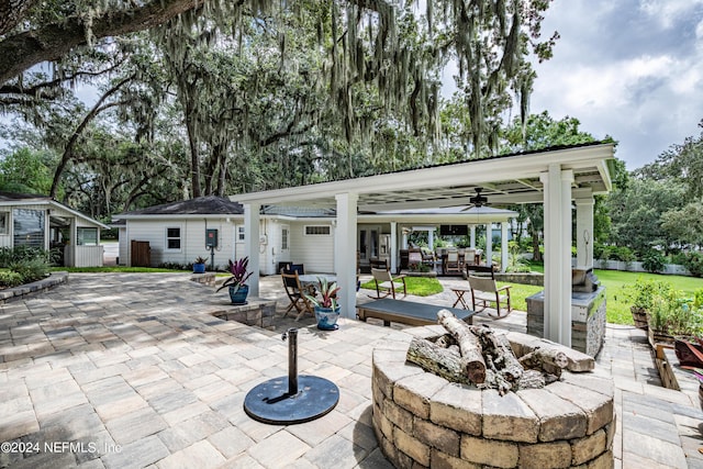 view of patio / terrace featuring an outdoor fire pit, an outdoor structure, outdoor dining space, and ceiling fan