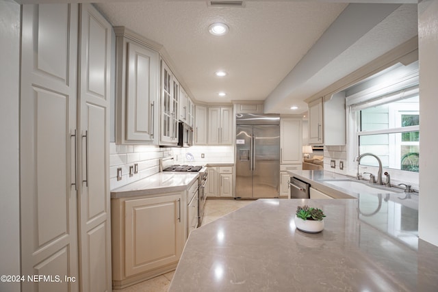 kitchen featuring light countertops, decorative backsplash, glass insert cabinets, a sink, and high quality appliances