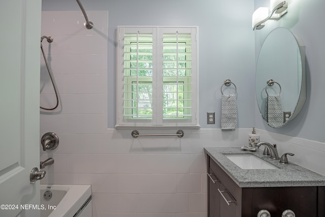 bathroom featuring tiled shower / bath combo, plenty of natural light, vanity, and tile walls