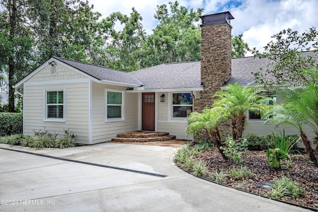 view of front of home featuring a shingled roof, driveway, and a chimney