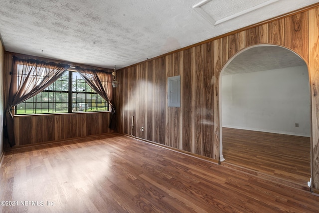 unfurnished room featuring dark hardwood / wood-style flooring, wooden walls, a textured ceiling, and electric panel