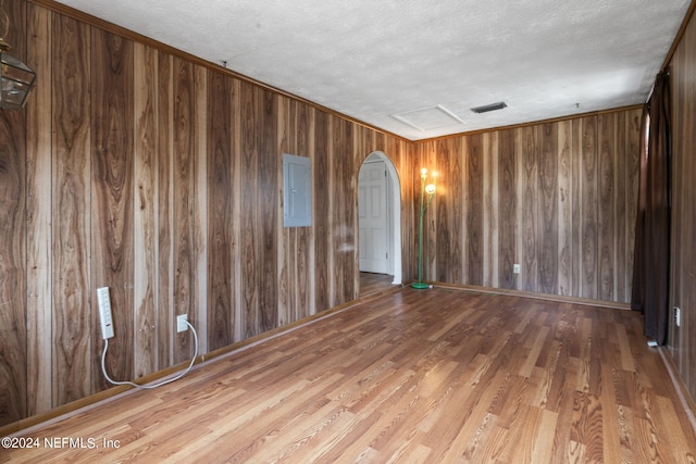 empty room featuring wooden walls, a textured ceiling, hardwood / wood-style floors, and electric panel