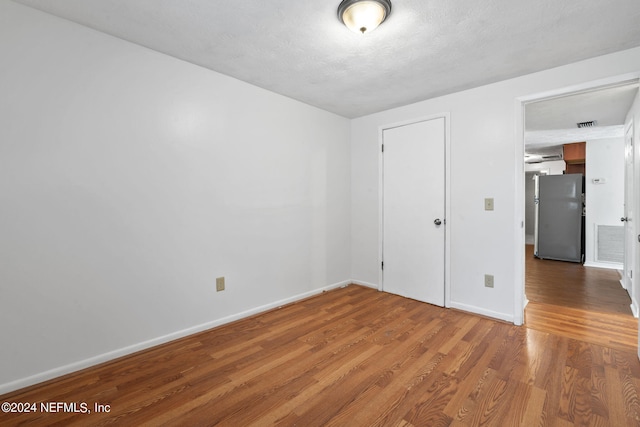 unfurnished bedroom with hardwood / wood-style flooring, stainless steel refrigerator, and a textured ceiling