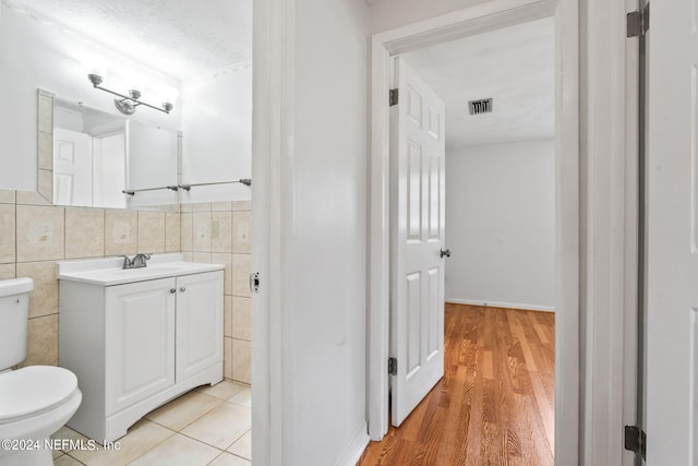 bathroom with tile walls, toilet, hardwood / wood-style floors, and vanity