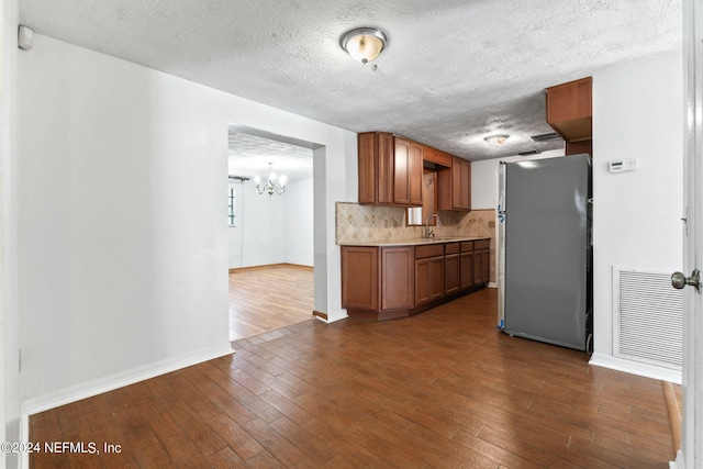 kitchen featuring dark wood-type flooring, tasteful backsplash, stainless steel refrigerator, sink, and a notable chandelier