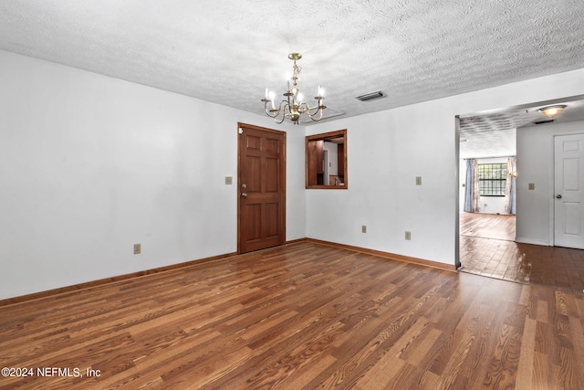 spare room featuring a textured ceiling, a notable chandelier, and hardwood / wood-style floors