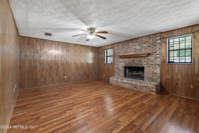 unfurnished living room featuring a fireplace, wooden walls, dark wood-type flooring, and brick wall